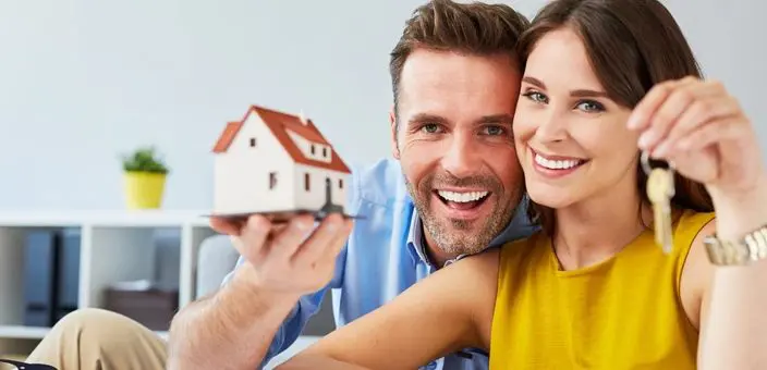 A woman and a man smiling holding a home model and keys