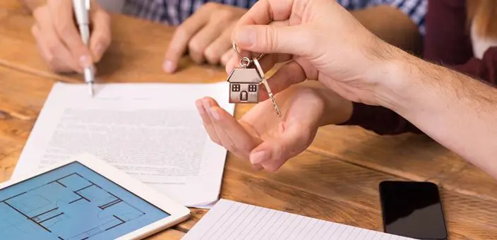 A person holding keys to a house on top of papers.