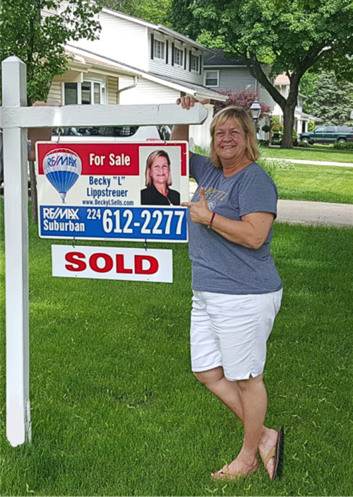 A woman standing next to a sold sign.